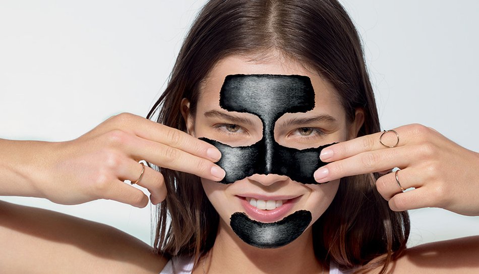 Lachende vrouw met houtskool masker voor de vette huid 